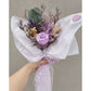 Small bunch of dried & preserved flowers in purple shades, green & cream and featuring a preserved purple rose. Wrapped ready for gifting. Pic shows bunch held up against a wall and zoomed in a bit closer