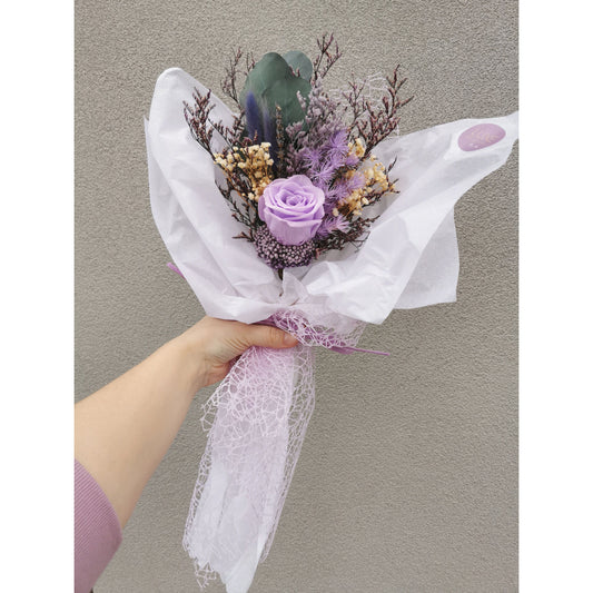 Small bunch of dried & preserved flowers in purple shades, green & cream and featuring a preserved purple rose. Wrapped ready for gifting. Pic shows bunch held up against a wall