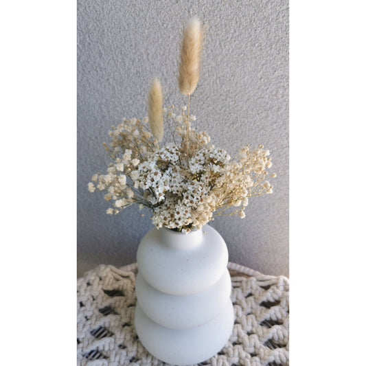 Cream, beige & white dried flowers in white bubble vase. Picture shows the arrangement sitting on a table against a blank wall.