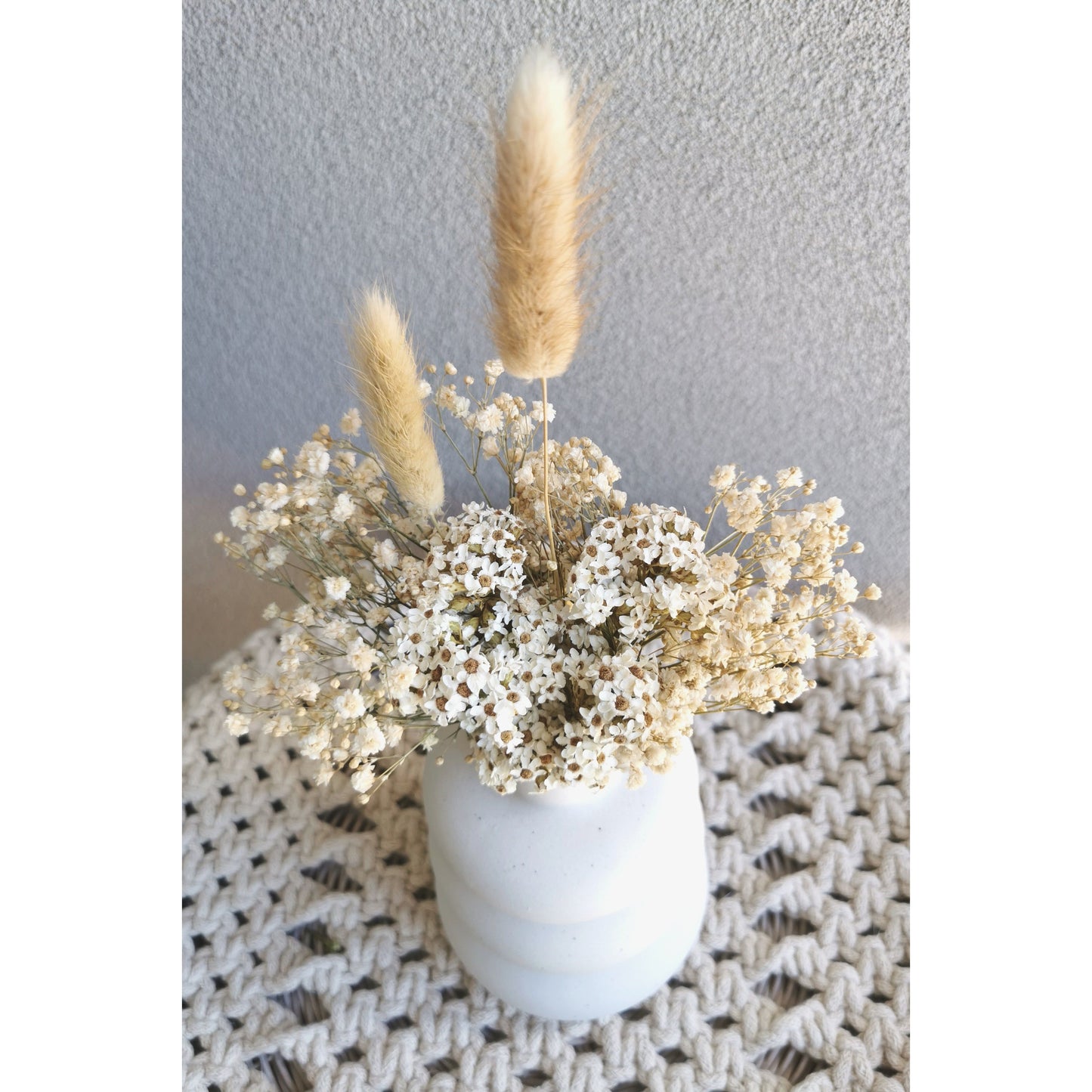 Cream, beige & white dried flowers in white bubble vase. Picture shows the arrangement sitting on a table against a blank wall with the view showing from the top