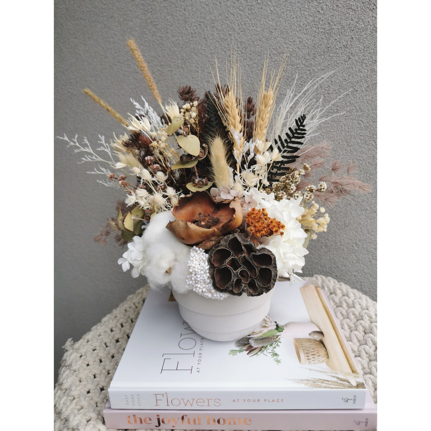 Dried & Preserved native flower arrangement in white pot. Picture shows flower arrangement sitting on a table against a blank wall