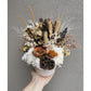 Dried & Preserved native flower arrangement in white pot. Picture shows flower arrangement being held up by hand against a blank wall