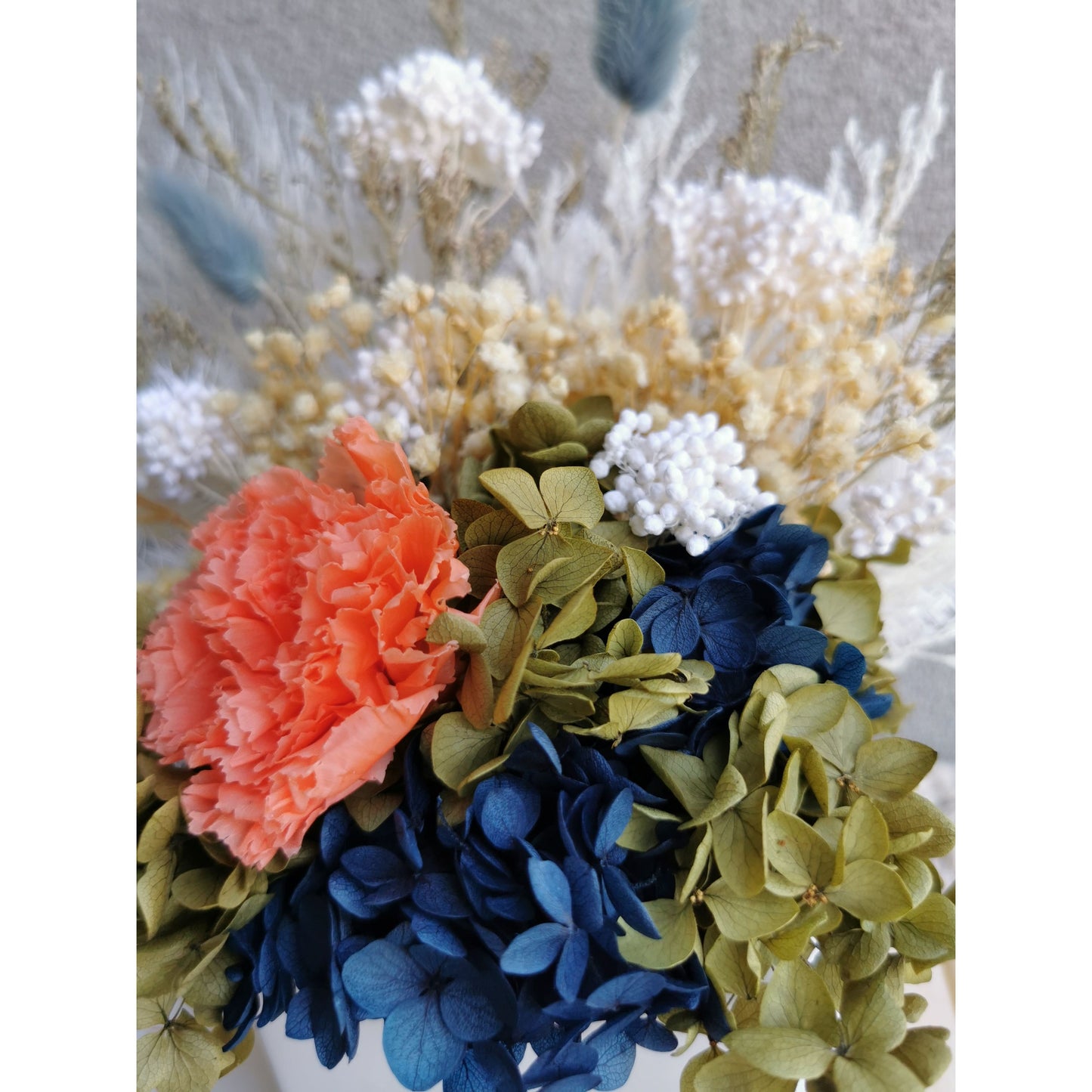 Dried & preserved flower arrangement with navy blue, green, white & orange flowers. Picture shows a close up view of the flowers and colours