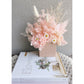Dried & Preserved flower arrangement in pretty pink with 3 white daisies. Flowers are set in to a mini pink arch vase. Picture is showing the arrangement sitting on top of books on a table