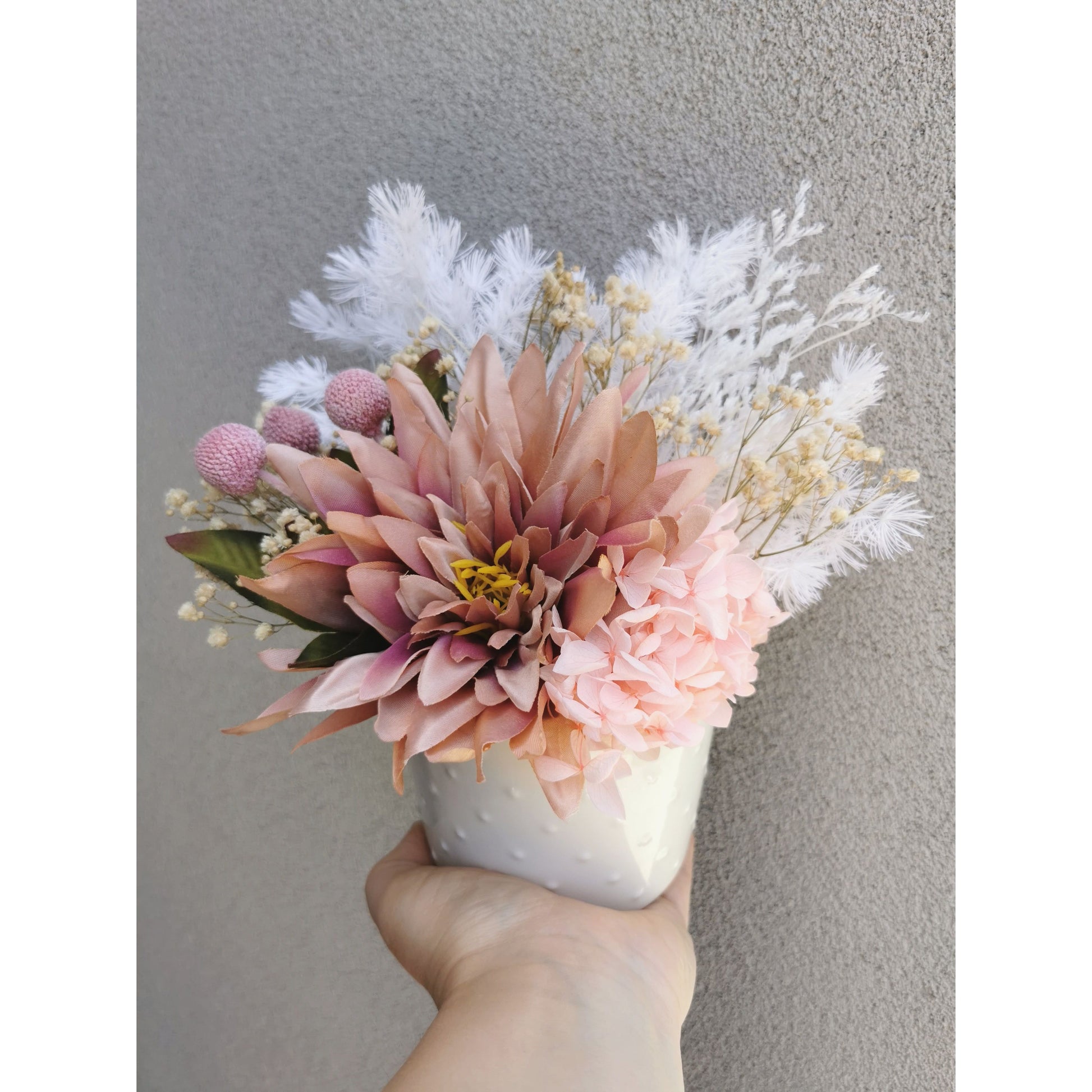 Dried & Preserved flower arrangement with silk artificial Dahlia flower. Photo shows arrangement being held by hand against a blank wall