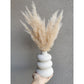 Plumes of soft pampas grass coming out of a white bubble vase. Photo shows pampas in vase being held by hand against a blank wall