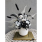 Black & White dried flower arrangement in white vase. Photo shows arrangement sitting on a book on a table against a blank wall