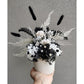 Black & White dried flower arrangement in white vase. Photo shows arrangement being held by hand against a blank wall