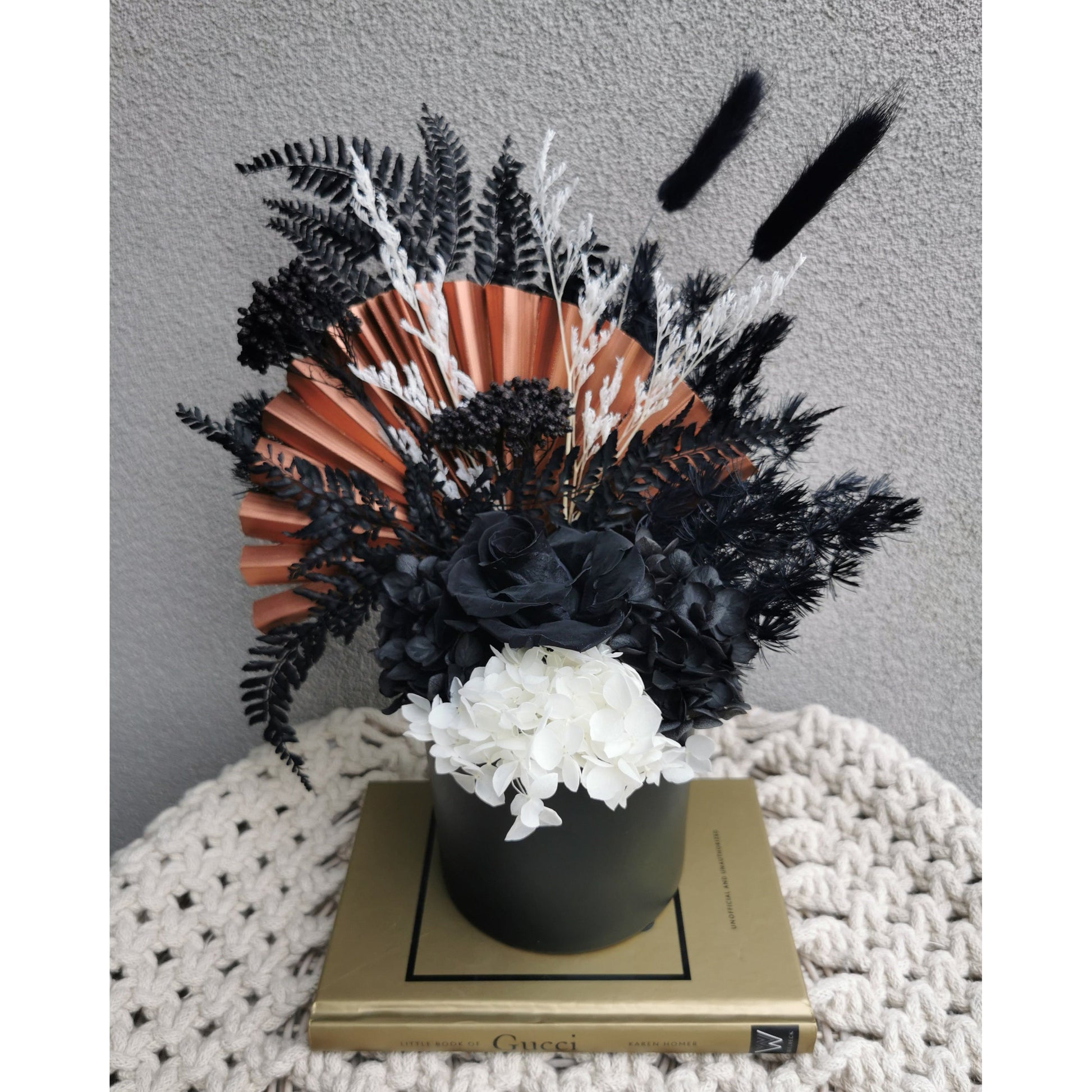 Dried & Preserved flower arrangement in black, white & copper colours. Photo shows arrangement sitting on a book on a table against a blank wall