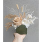 Dried & Preserved flower arrangement with nude and white flowers in a green mini arch vase. Picture shows arragement being held by hand against a blank wall