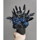 Navy Blue & Black Dried & Preserve Flowers in black vase. Photo shows flowers being held by hand against a blank wall