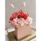 Valentines Day dried & preserved flower arrangement with red & pink flowers in pink arch vase. Photo shows arrangement sitting on books on an angle against a blank wall