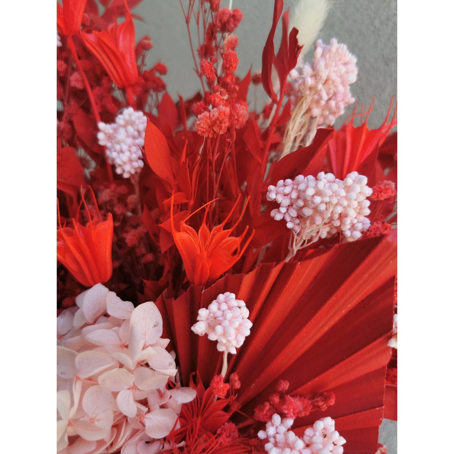 Bunch of Dried & Preserved flowers in red & pink colours and sitting in a frosted glass vase. Photo shows a close up of the flowers