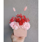 Valentines Day dried & preserved flower arrangement with red & pink flowers in pink arch vase. Photo shows arrangement being held by hand against a blank wall